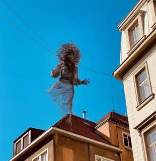 Ethereal figure hanging from street wires between two buildings as streetart